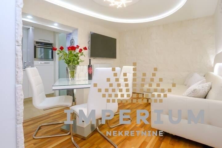 Modern studio apartment interior with white furniture, wooden floor, dining area with flowers, and mounted TV on wall