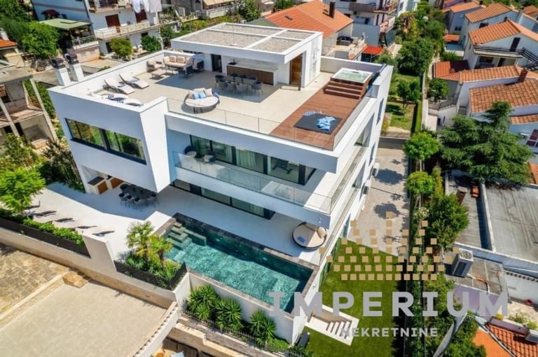 Aerial view of a modern white three-story residential house with a swimming pool and terrace surrounded by neighboring buildings
