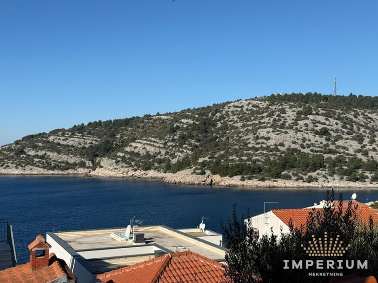 Coastal view with red-tiled rooftop terrace overlooking blue Mediterranean Sea and forested hillside