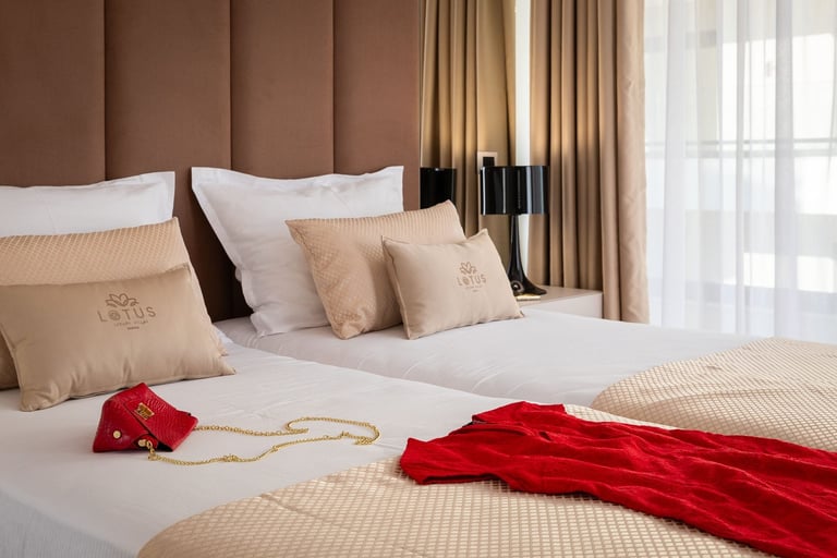 Luxurious bedroom with neutral tones featuring a bed with decorative red fabric draped across it and small red accessory on white linens