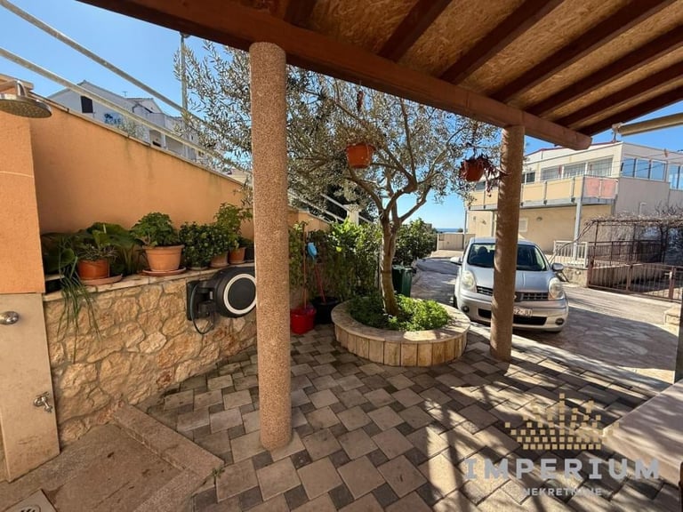 Covered patio area with stone walls, wooden pergola, potted plants, and shaded seating overlooking parked vehicles and urban street