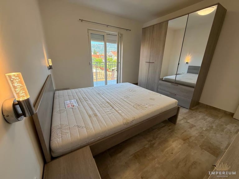 Spacious modern bedroom with queen bed, mirrored wardrobe, wooden flooring, glass balcony door, and wall sconces