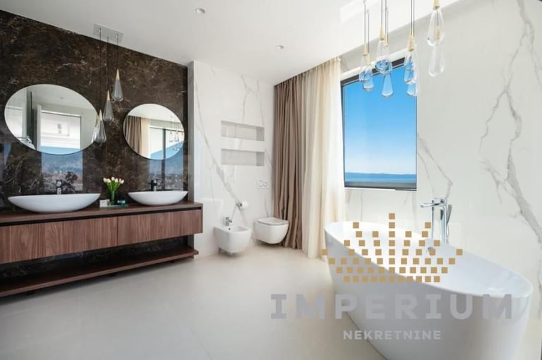 Modern luxury bathroom with dual round mirrors, marble accents, freestanding bathtub, and ocean view through large window