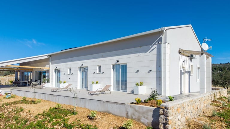 Modern white prefab house with large windows and covered terrace under clear blue sky