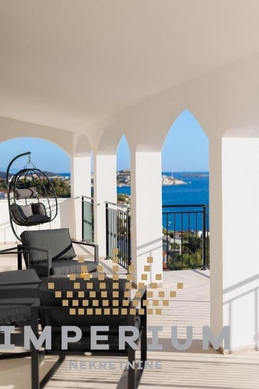 Modern white terrace with hanging chair overlooking blue sea and coastal cliffs through arched windows