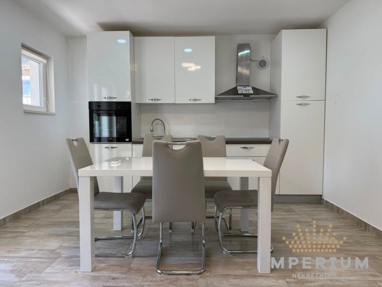 Modern kitchen and dining area with white cabinetry, stainless steel range hood, white dining table, and upholstered chairs