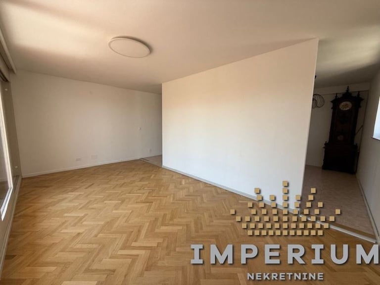 Empty room with herringbone wood flooring, white walls, and stacked boxes on the floor, with Imperium watermark