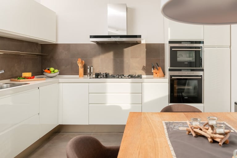 Modern white kitchen with stainless steel appliances, brown backsplash, and wooden dining table