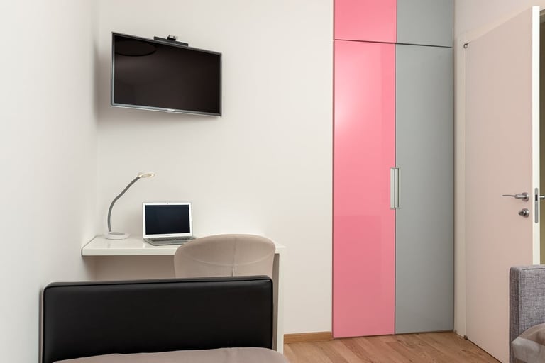 Modern bedroom with wall-mounted TV, laptop on nightstand, black bed frame, and pink and gray wardrobe closet