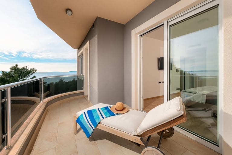 Modern balcony with lounge chair, ocean view, glass doors, and coastal scenery