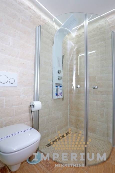 Modern bathroom with glass shower enclosure, white toilet, and beige tiled walls with LED lighting