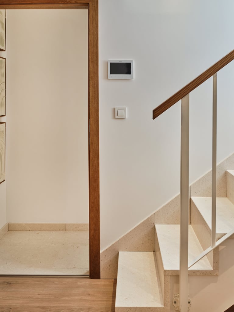 Modern staircase with wooden handrail and light wood treads next to an open doorway with thermostat on white wall