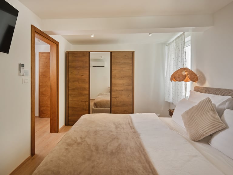 Modern bedroom with wooden wardrobe, bed with neutral bedding, pendant lamp, and hardwood flooring throughout the contemporary space