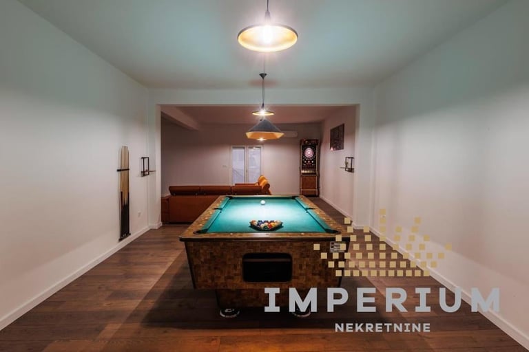 Modern game room with turquoise billiard table, wooden flooring, pendant lights, and white walls with dark wood accents