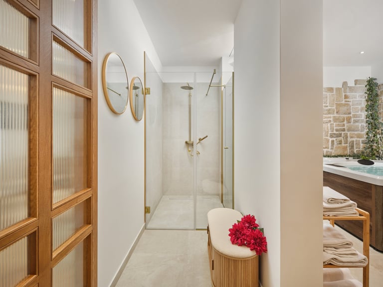 Modern bathroom interior with glass shower enclosure, wooden cabinetry, round mirrors, and red flowers on vanity