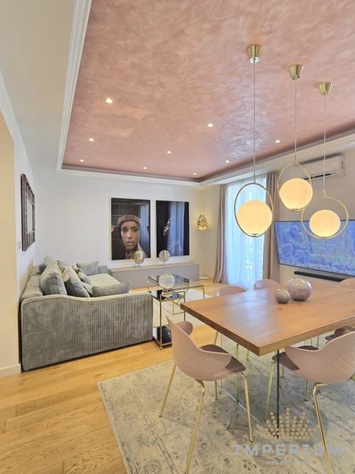 Modern living room and dining area with wooden floors, gray sofa, wood dining table, pendant lights, and pink tray ceiling