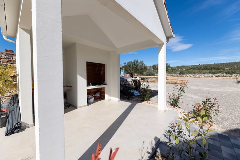 Modern white house patio with open-sided covered area overlooking rural landscape under clear blue sky
