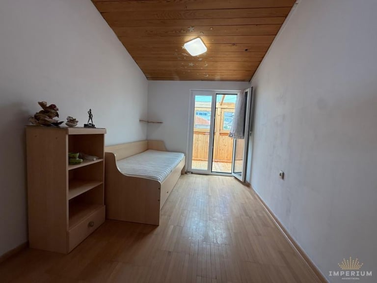 Minimalist bedroom with wooden floor, brown ceiling, single bed, wooden shelving, and glass doors leading to a balcony