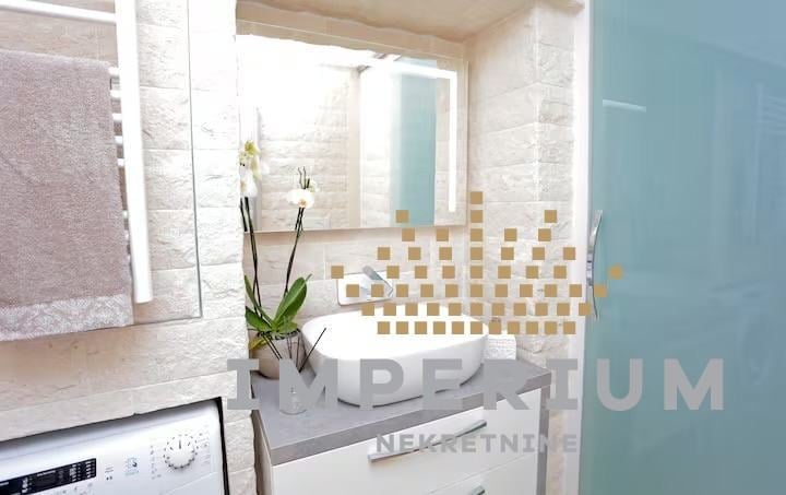 Modern bathroom interior with white fixtures, geometric gold tile accents, mirror with lighting, and potted orchid plant