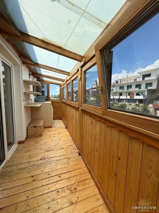 Bright enclosed wooden balcony with glass roof panels and windows overlooking residential buildings