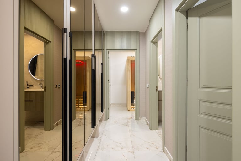 Modern hallway with mirrored closet doors, marble flooring, white ceiling, and neutral wood cabinetry on both sides
