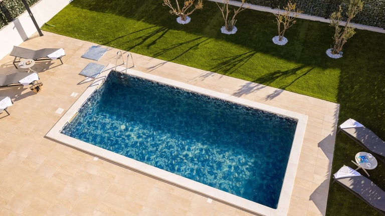 Overhead view of rectangular swimming pool surrounded by tan patio and green lawn with lounge chairs
