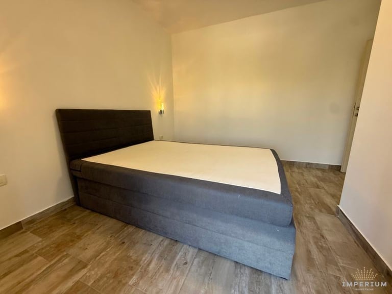 Modern bedroom with a dark blue upholstered bed frame and white mattress on wooden flooring in a minimalist apartment