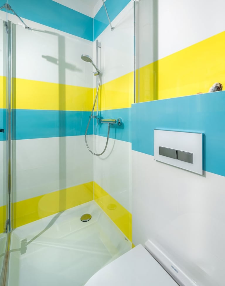 Modern bathroom shower with colorful horizontal stripes in turquoise, yellow, and white, featuring glass enclosure and chrome fixtures