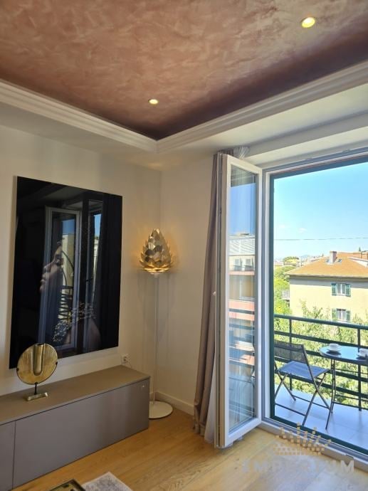 Modern bedroom with textured tray ceiling, vanity with mirror, gold wall sconce, and glass doors opening to balcony with city view