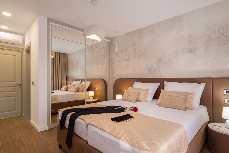 Modern bedroom with white bed, large mirror, warm lighting, and wooden flooring in a contemporary hotel or apartment interior