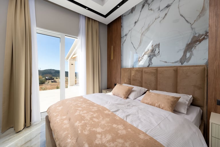 Modern bedroom with king-size bed, marble accent wall, beige upholstered headboard, and floor-to-ceiling windows with valley view