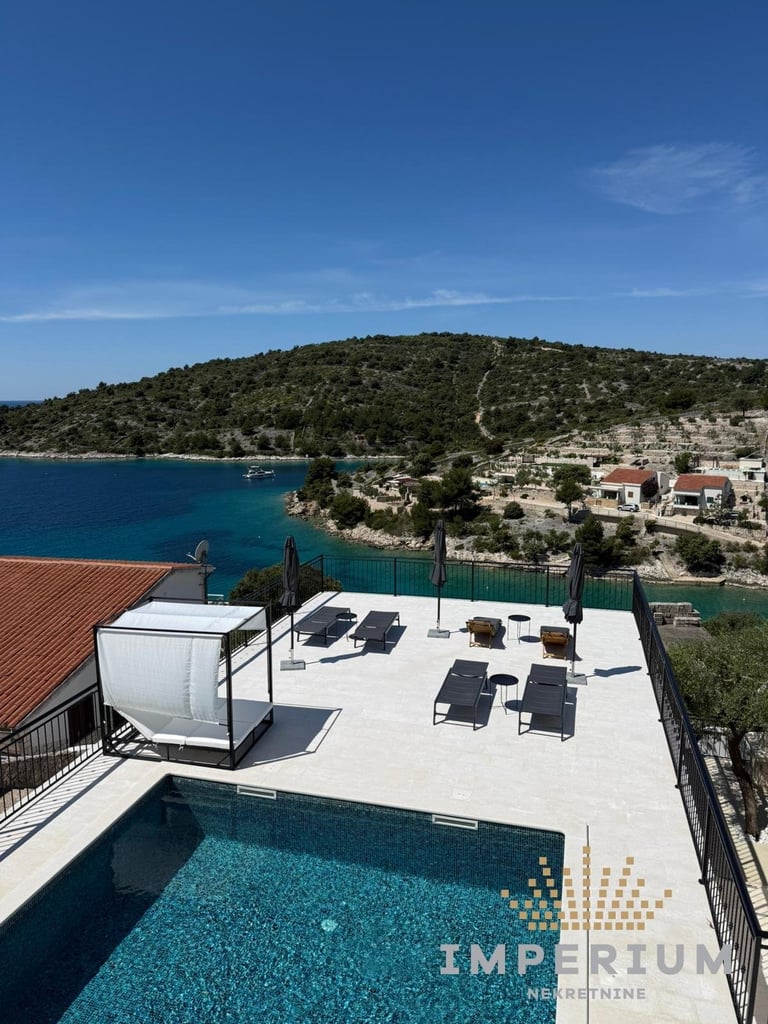 Luxury rooftop pool with turquoise water, loungers, and panoramic view of Mediterranean coastline with forested hillside and waterfront village