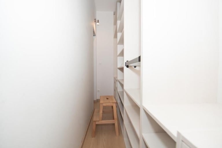 Narrow hallway with white walls, wooden stool, and built-in shelving along the right side