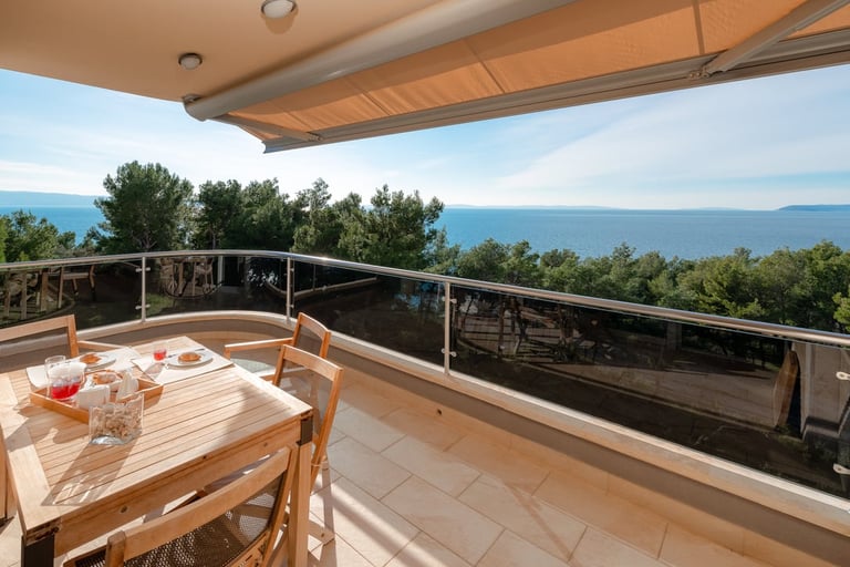 Modern terrace with dining table overlooking ocean and mountains under a retractable sunshade