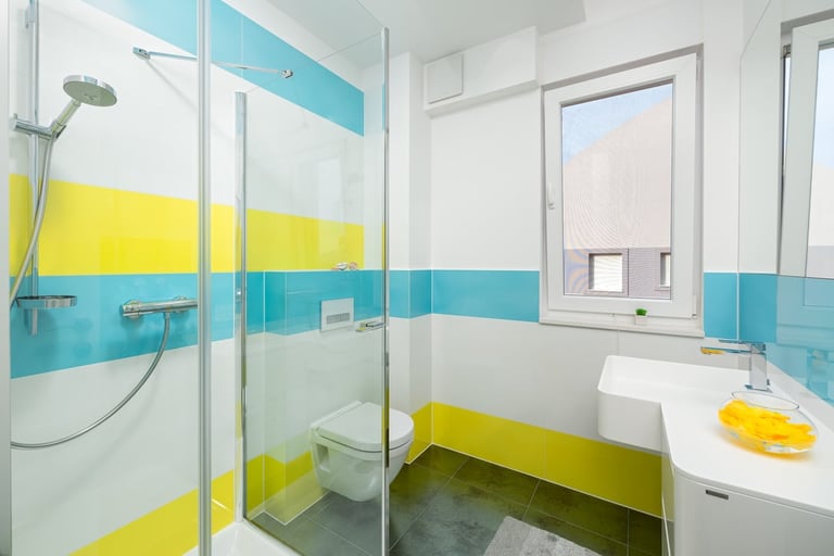 Modern bathroom with turquoise and yellow tile accents, glass shower enclosure, white sink, and window