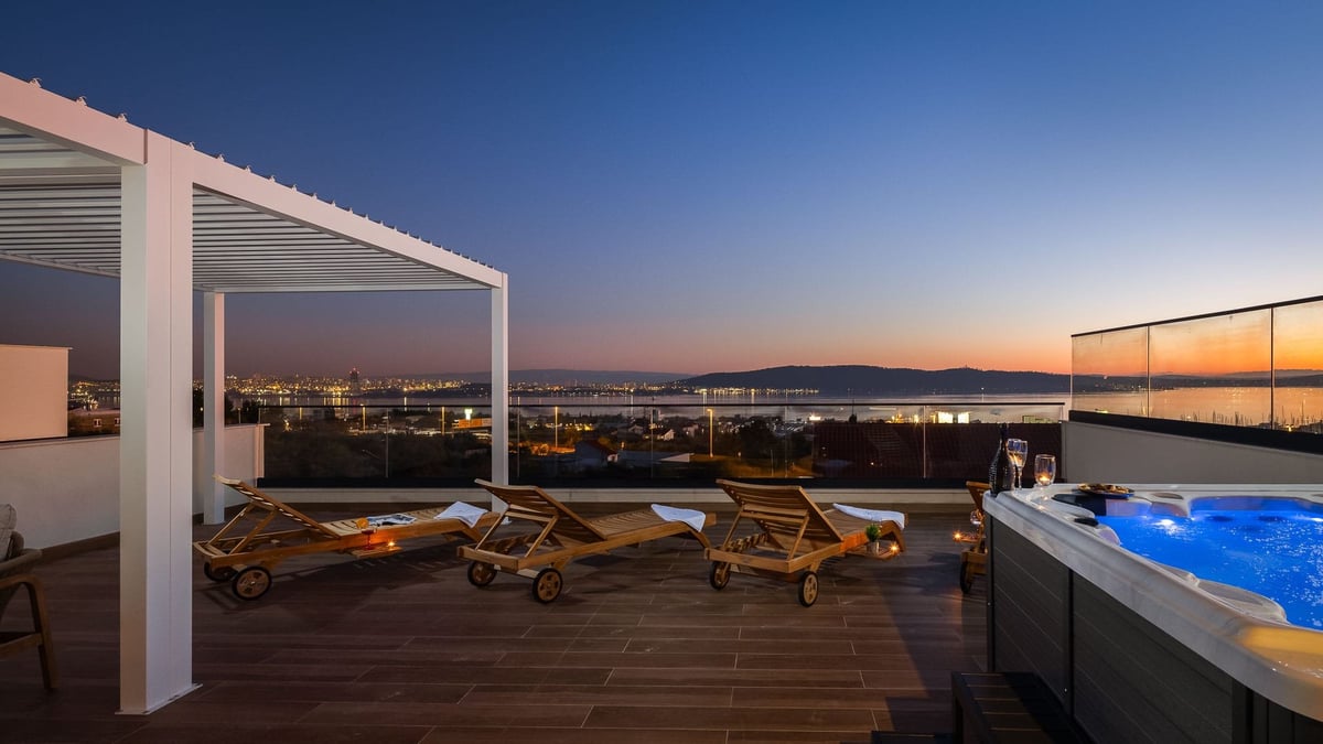 Modern rooftop terrace at dusk with lounge chairs, pergola, infinity pool, and panoramic city and water views at sunset