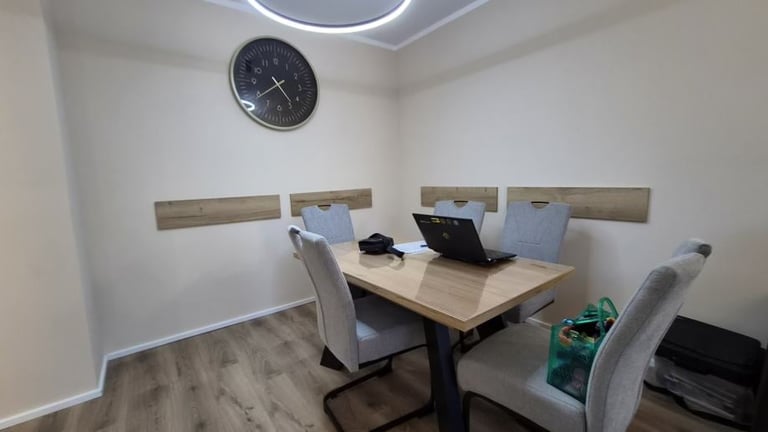Modern office space with desk, two gray chairs, laptop, and wall-mounted shelving under a round ceiling light