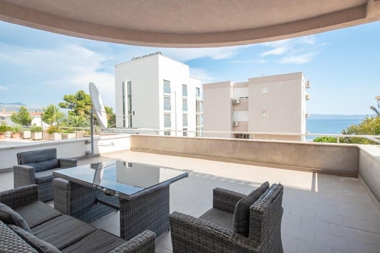 Modern balcony terrace with rattan furniture overlooking contemporary white building and sea horizon