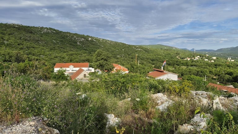 Rural settlement nestled in green hills with red-roofed buildings surrounded by lush vegetation and rocky terrain