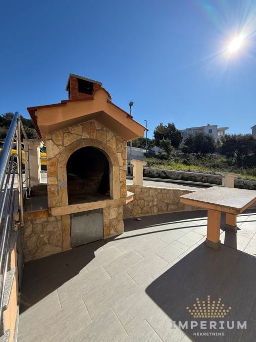 Stone outdoor pizza oven with arched opening on a patio area with tables and hillside view under clear blue sky