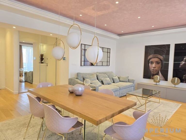 Modern living room with wooden dining table, pink chairs, green sofa, brass pendant lights, and pink ceiling