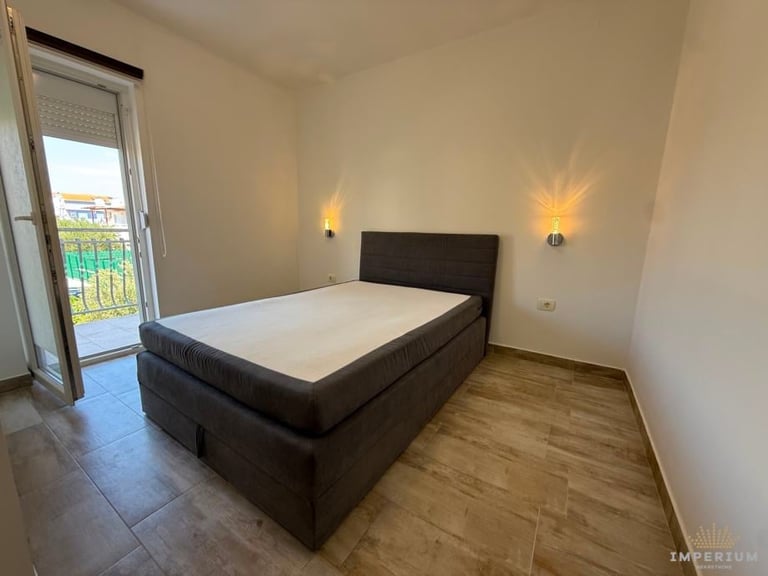 Modern bedroom with black bed, wooden floor, beige walls, wall sconces, and balcony access through glass doors