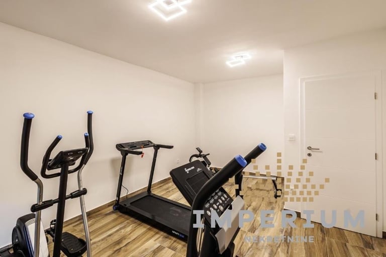 Home gym with cardio equipment including stationary bike, treadmill, and exercise machine on wooden floor