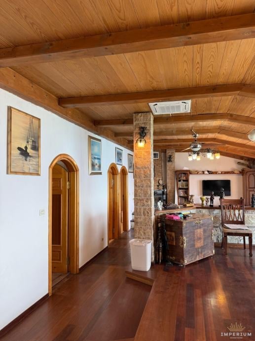Spacious wooden interior hallway with exposed beam ceiling, arched doorways, and open-plan living areas visible in background