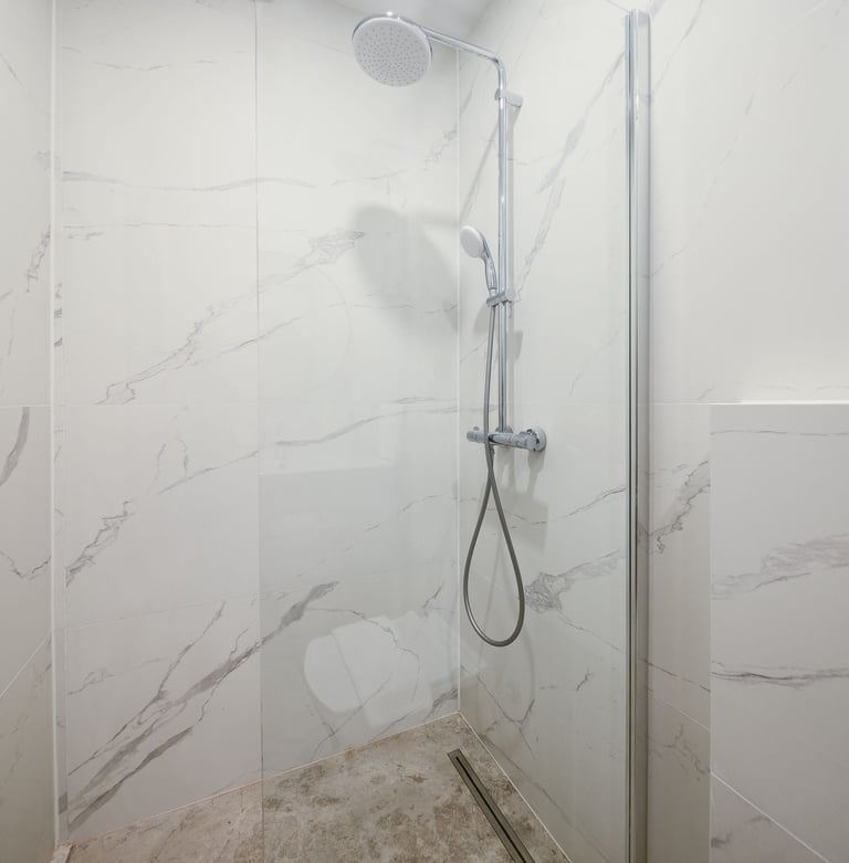 Modern shower enclosure with marble-effect wall tiles, chrome fixtures, handheld showerhead, and glass door panel