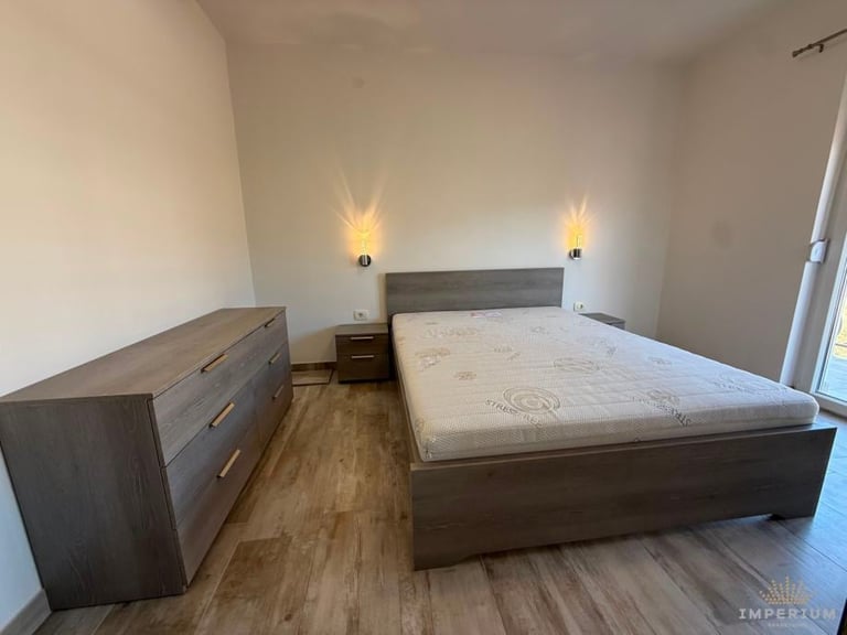 Modern bedroom with dark wood bed frame, matching dresser, wall-mounted sconces, and wooden flooring