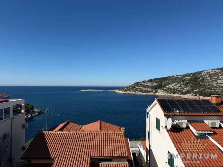 Elevated view of Mediterranean coastal village with terracotta-roofed buildings overlooking blue sea and hillside