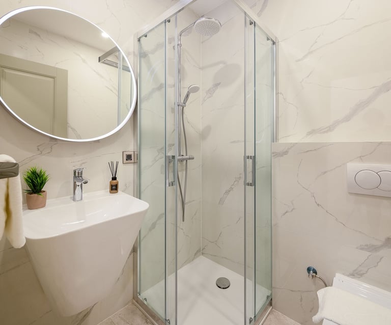 Modern bathroom with marble-look tiles, glass shower enclosure, white curved sink with round mirror, and minimalist decor