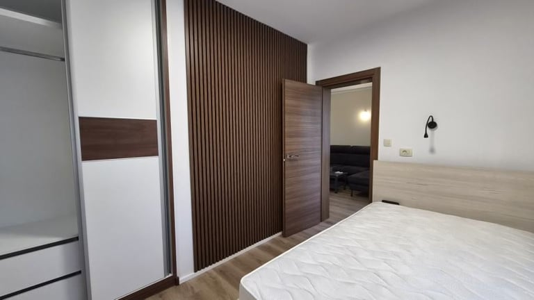Modern bedroom with white bed, brown wooden accent wall, wardrobe, and open door leading to ensuite bathroom