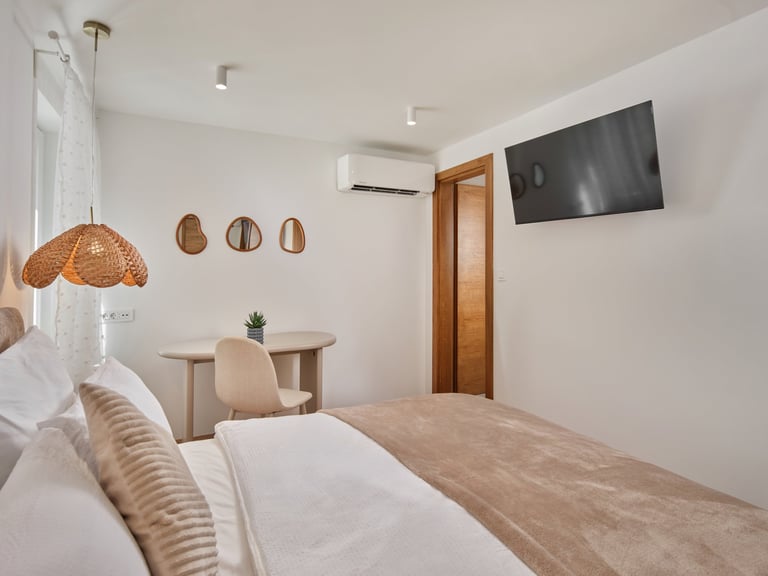 Modern bedroom with wooden bed, rattan pendant light, wall-mounted TV, desk area, and minimalist decor in neutral tones